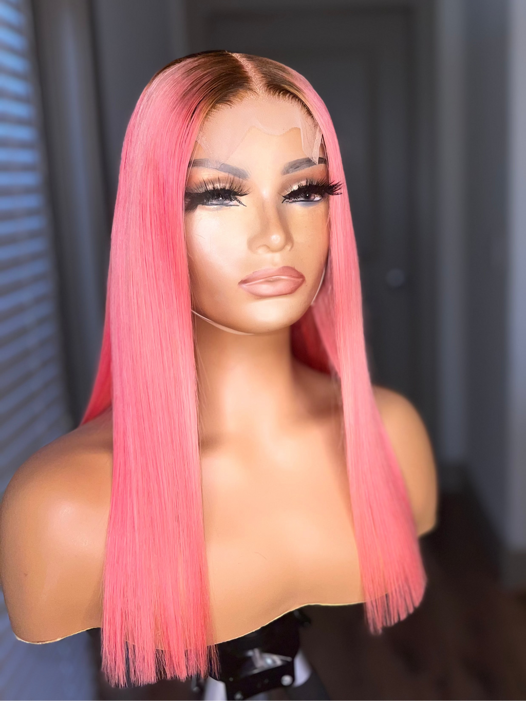 Mannequin head with pink straight wig against a neutral background
